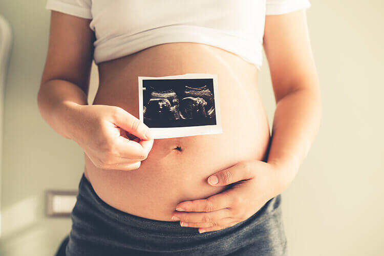 close up of a lady holding an ultrasound picture in front of her pregnant belly