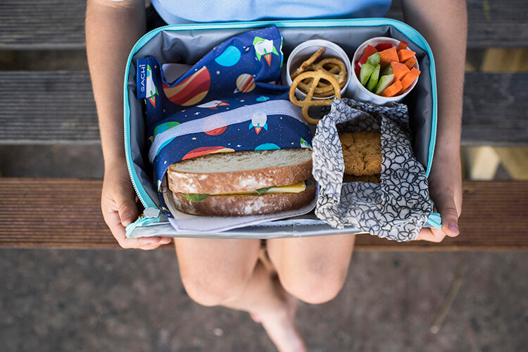 An open lunchbox showing fresh food wrapped in cloth or in reusable cups