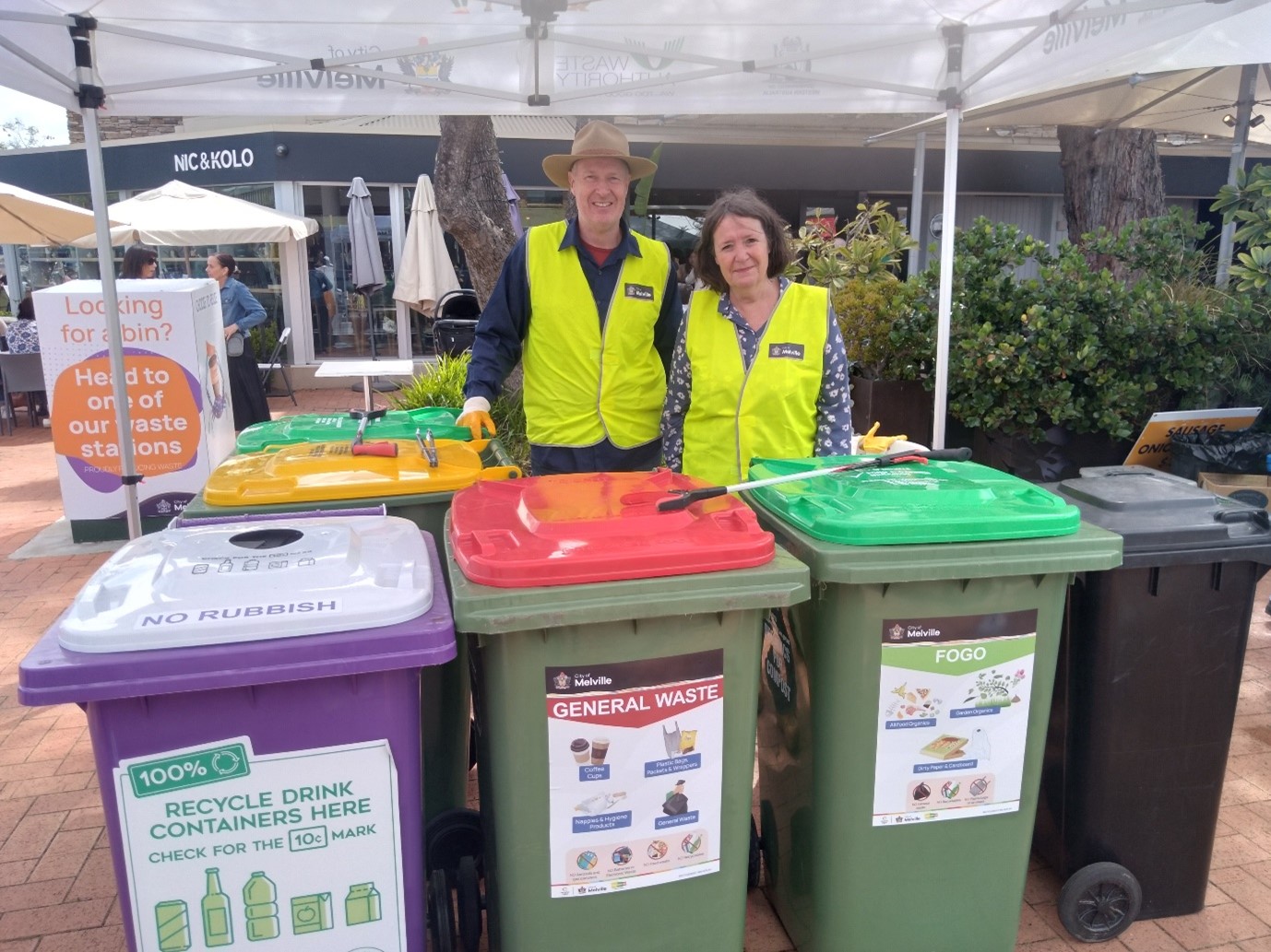 Photo of two people in hi-res clothing behind a collection of waste bins