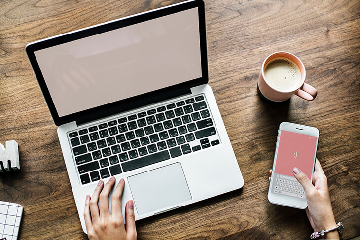 close up of a desk scene comprising of a laptop, smartphone and coffee cup