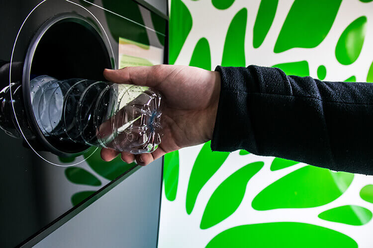 Close up of hand depositing an empty drink container into a machine