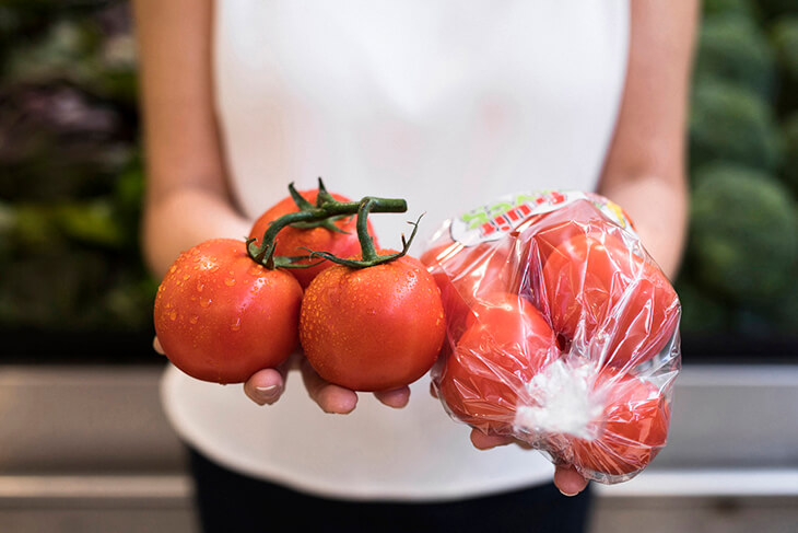 close up of hands holding plastic wrapped tomatoes and no-wrapped ones