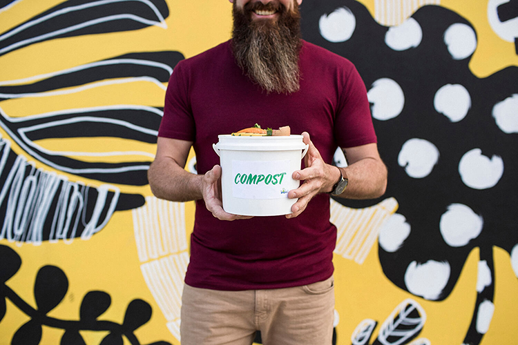 Man holding a bucket of scraps labeled compost