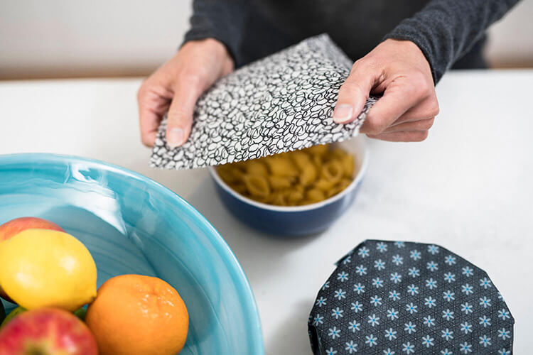 close up of hands covering a bowl with a reusable cover