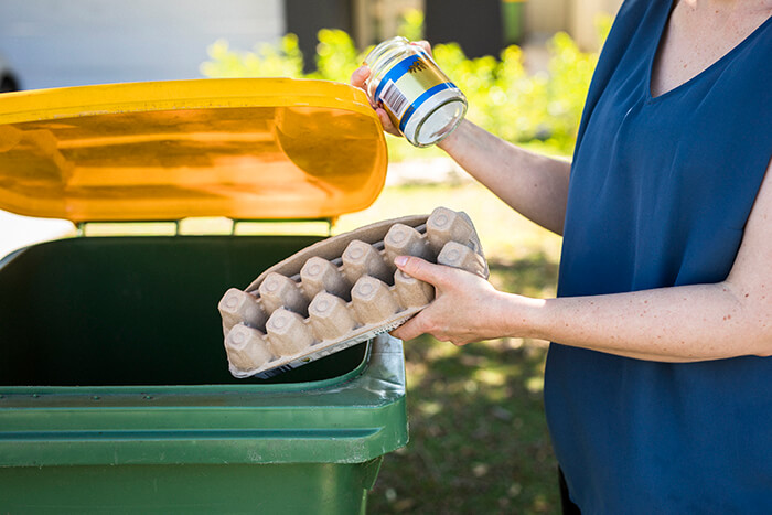 lady placing an egg carton in a recycling bin